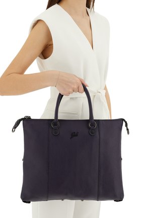 Donna con abito bianco senza maniche che tiene una grande borsa tote in pelle viola scuro per i manici di lato.