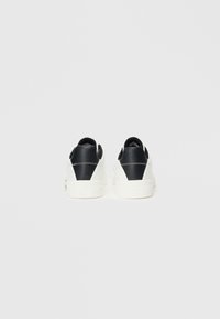Witte sneakers met een zwarte leren hak en getextureerde accenten. Minimalistisch ontwerp, ronde vorm en witte rubberen zolen.