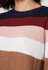 Stickad tröja med breda horisontella ränder i marinblått, burgundy, rosa, vitt och brunt, med en texturerad ribbad design och rund halsringning.