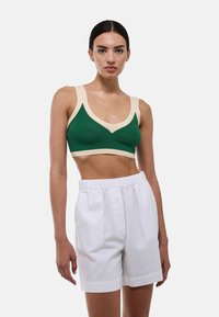 Bralette vert à côtes avec des accents beiges ; design en V ; associé à un short blanc taille haute, avec une taille élastique et des plis.