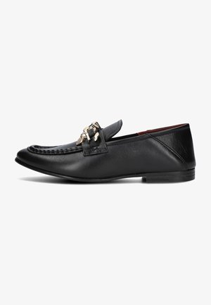 Mocassin en cuir noir avec détail de chaîne dorée, couture moc toe, et talon plat bas, vu de côté sur un fond blanc.