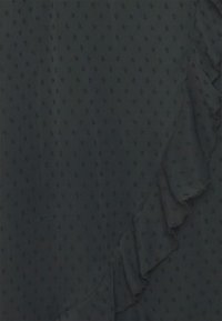 Tecido verde escuro com pequenos pontos texturizados. O volante lateral adiciona dimensão à borda, criando uma aparência em camadas.