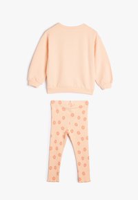Sudadera de melocotón con mangas acampanadas y dobladillo acanalado combinada con leggings acanalados a juego en melocotón que presentan un patrón de flores.