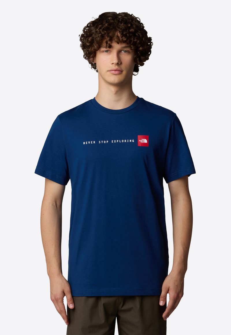 Camiseta de algodón de color azul marino con un estampado de texto blanco que dice "NUNCA DEJES DE EXPLORAR" y un pequeño logotipo cuadrado rojo en el lado izquierdo del pecho. Manga corta.