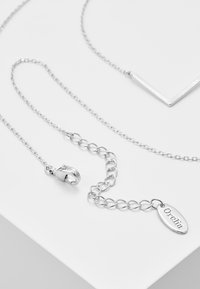 Collana di argento con pendente a forma di chevron, catena con anelli testurizzati e chiusura con un'etichetta incisa "Orelia."