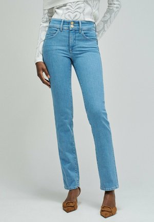 Vaqueros azul claro ajustados con cierre de doble botón, combinados con tacones puntiagudos marrones y una camiseta blanca estampada.