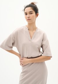 Beiges Kurzarmkleid mit V-Ausschnitt und lockerer Passform, aus glattem Stoff; Highlights sind dezente Nähte und seitliche Details.