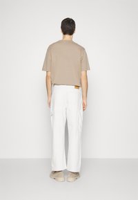 Camiseta beige de manga corta combinada con pantalones cargo de pierna ancha blancos. Los pantalones cuentan con bolsillos laterales y una etiqueta de cuero marrón en la parte trasera.