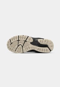Black athletic shoe sole with textured grooves, featuring a beige rubber outsole and a distinct wavy design along the midsection.