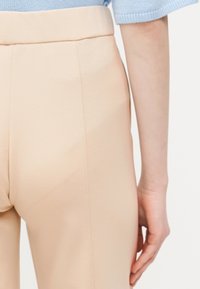 Κοντινό πλάνο ατόμου που φοράει μπεζ παντελόνι ψηλής μέσης και ανοιχτό μπλε κοντομάνικο τοπ, δείχνοντας πλαϊνή και πίσω όψη από τη μέση έως το χέρι.