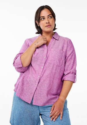 Helles Pink, kurzärmliges Hemd aus strukturiertem Stoff mit Kragen, einer Brusttasche und hochgekrempelten Ärmeln, kombiniert mit Denim-Shorts.