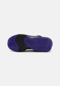 Semelle de chaussure noire avec des accents violets, présentant des motifs texturés pour l'adhérence, et une surface lisse. Logo Nike notable dans un design épuré.