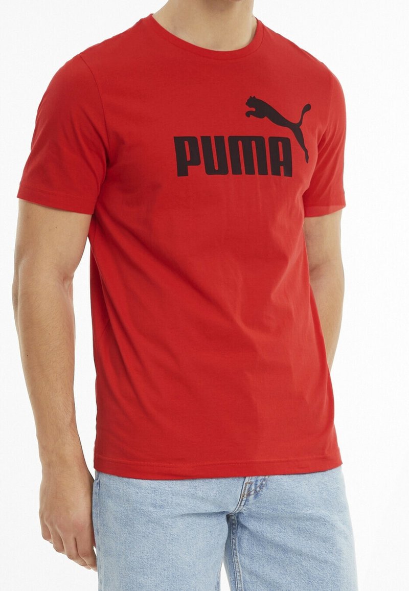 Homme portant un t-shirt rouge Puma avec un logo noir et un jean bleu clair, torse et parties supérieures des jambes visibles.