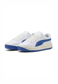 Weiße und blaue Sneakers mit perforierten Details, Obermaterial aus glattem Leder, flachen weißen Schnürsenkeln und einer blauen Gummisohle. PUMA-Logo an der Seite.