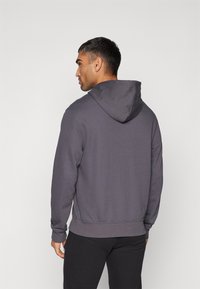 Sweatshirt à capuche grise avec une coupe décontractée, featuring un cordon de serrage et des poignets côtelés, porté sur un pantalon noir.