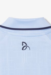 Ljusblå polo med mörkblå krage och en svart logo på ryggen, med ett strukturerat geometriskt mönster.