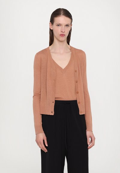 Rust-colored cardigan with a V-neckline, ribbed cuffs, and a button front design, paired with a matching top and loose black trousers.