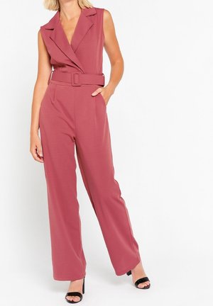 Combinaison sans manches rose framboise avec taille ceinturée, coupe ajustée, jambes larges et revers crantés. Tissu lisse avec une texture minimale.