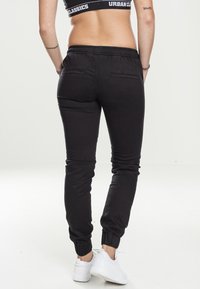 Svarta joggers med elastisk midja och mudd, med en slät textur och bakfickor, kombinerat med vita sneakers.