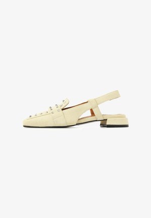 Chaussure plate slingback en daim beige avec bout carré, clous argentés sur le dessus, et petit talon bloc avec semelle noire.
