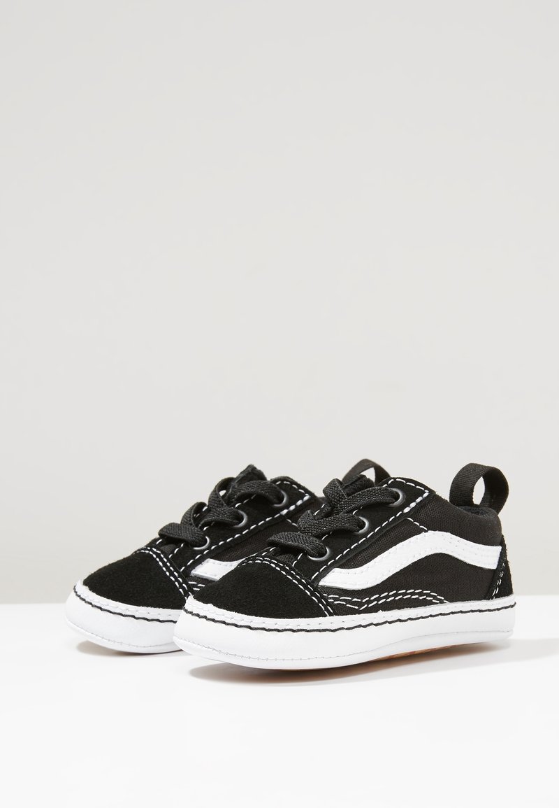Petites baskets noires et blanches pour tout-petits avec des lacets et une bande blanche ondulée sur le côté, placées côte à côte sur une surface claire et plane.