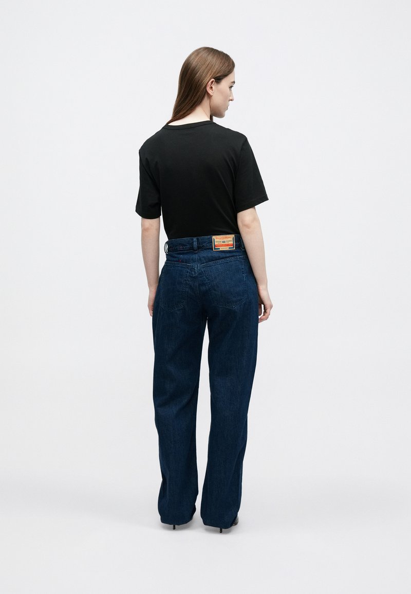 Sort t-shirt med korte ærmer kombineret med blå straight-leg jeans, der har et tekstureret stof og en synlig mærkeetiket på taljebåndet.