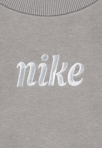 Sivi dukserica izrađena od teksturiranog materijala s izvezenim bijelim "nike" logotipom na sredini prsnog dijela. Rebrasti izrez.