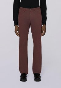 Bordeauxfarbene Jeans mit geradem Bein, aus strukturiertem Stoff, im Fünf-Taschen-Design und mit Druckknopfverschluss, kombiniert mit schwarzen, polierten Schuhen.