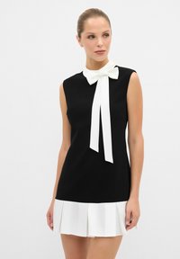 Schwarzes ärmelloses Kleid mit weißem Schleifenkragen und weißem Faltensaum. Glattes Material mit klaren Linien und einer taillierten Silhouette.