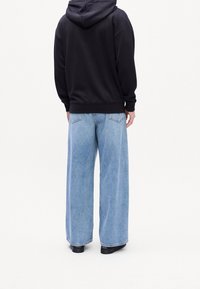 Černá mikina s kapucí a světle modré široké džíny. Materiál působí měkce; džíny mají vybledlý vzhled s viditelnými zadními kapsami a švy.