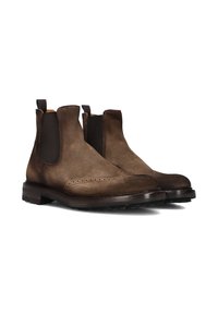 Bottines Chelsea en daim marron avec panneaux élastiques sur les côtés, perforations brogue détaillées et semelle en caoutchouc. Texture lisse avec une forme de bout arrondi.
