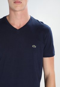 Navy blue cotton V-neck t-shirt featuring a small embroidered green crocodile logo on the left chest area. Short sleeves, fitted design.