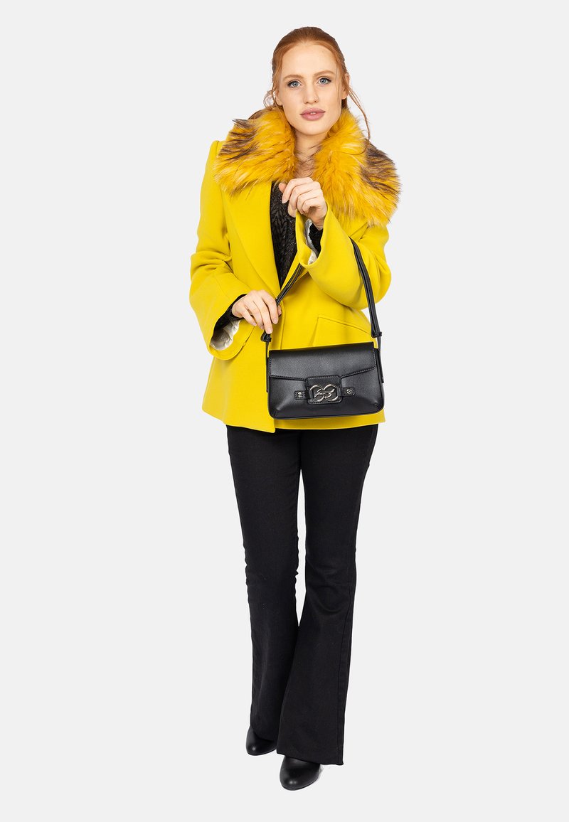 Cappotto giallo con collo in pelliccia sintetica, maglione nero, pantaloni neri a campana, borsa nera con hardware in argento, scarpe nere eleganti.