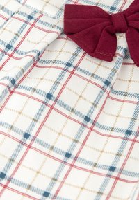Tissu en coton avec un fond blanc et un motif à carreaux bleu, rouge et jaune ; un accent en nœud bordeaux positionné à droite.