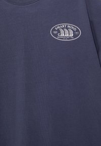 Chemise bleu marine avec un logo ovale blanc montrant trois léopards assis, texte "SMART MIND," "BROOKLYN/NYC/3743," et "EST. 1991"