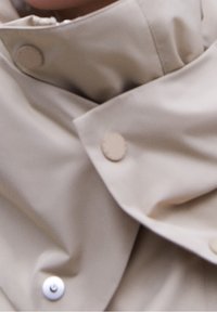 Primo piano di tessuto beige con bottoni automatici, che mostra sezioni abbottonate e non abbottonate e morbide pieghe.
