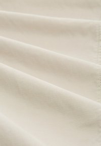 Cremfarbener Stoff mit einer strukturierten Webart, gefaltet, um glatte, diagonale Linien und subtile Oberflächendetails zu zeigen.