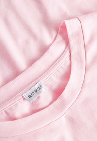 Lichtroze katoenen T-shirt met een ronde halslijn, een soepele textuur en een wit label met "RÖSCH" prominent gestikt.
