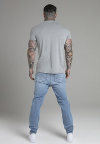 Grijze korte mouwen t-shirt gecombineerd met lichtblauwe spijkerbroeken en witte sneakers. De outfit heeft een aansluitend ontwerp en een soepele textuur.