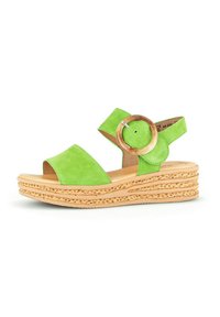 Green suede wedge sandal with a wide strap and circular wooden accent, featuring a textured woven sole and open toe design.