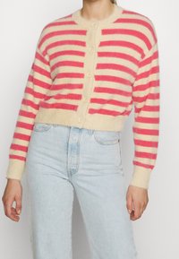 Červeno-krémový pruhovaný kardigan vyrobený z měkkého, chlupatého materiálu, s kulatým výstřihem, masivními knoflíky a zkráceným střihem s ribbovými manžetami.