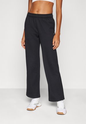 Black wide-leg sweatpants with an elastic waistband, made of soft fabric. Paired with white athletic shoes featuring light gray accents.