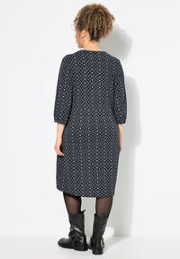 Navy Kleid mit einem geometrischen weißen Muster, drei Viertelärmeln und einem lockeren Schnitt. Kombiniert mit schwarzen Motorradstiefeln.