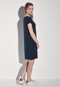 Krótka, granatowa sukienka z miękkiego materiału, z krótkimi rękawami i prostym krojem, zestawiona z białymi trampkami. Minimalistyczny design bez wzorów.