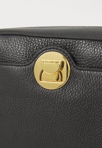 Black leather bag featuring a textured surface, gold circular clasp, and embossed brand name "Coccinelle" on the clasp.
