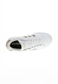 Zapatilla deportiva blanca con un patrón de leopardo en el talón, tres franjas blancas y el logo "cloudfoam comfort" en dorado.
