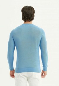 Pull en tricot bleu avec un col rond côtelé, un tissu texturé et des manches ajustées. Vue de dos, montrant l'ourlet et les détails.