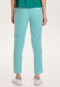 Gestreepte teal broek met een slim fit, met contrasterende verticale witte strepen en een eenvoudig ontwerp van de achterzak. Gemaakt in combinatie met witte sneakers.