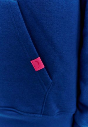 Tmavě modrá mikina vyrobená ze směsového bavlněného materiálu. Má přední kapsu a malou růžovou visačku s grafickým detailem. Hladký povrch.