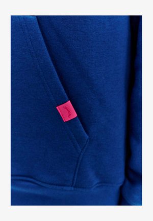 Tmavě modrá mikina vyrobená ze směsového bavlněného materiálu. Má přední kapsu a malou růžovou visačku s grafickým detailem. Hladký povrch.